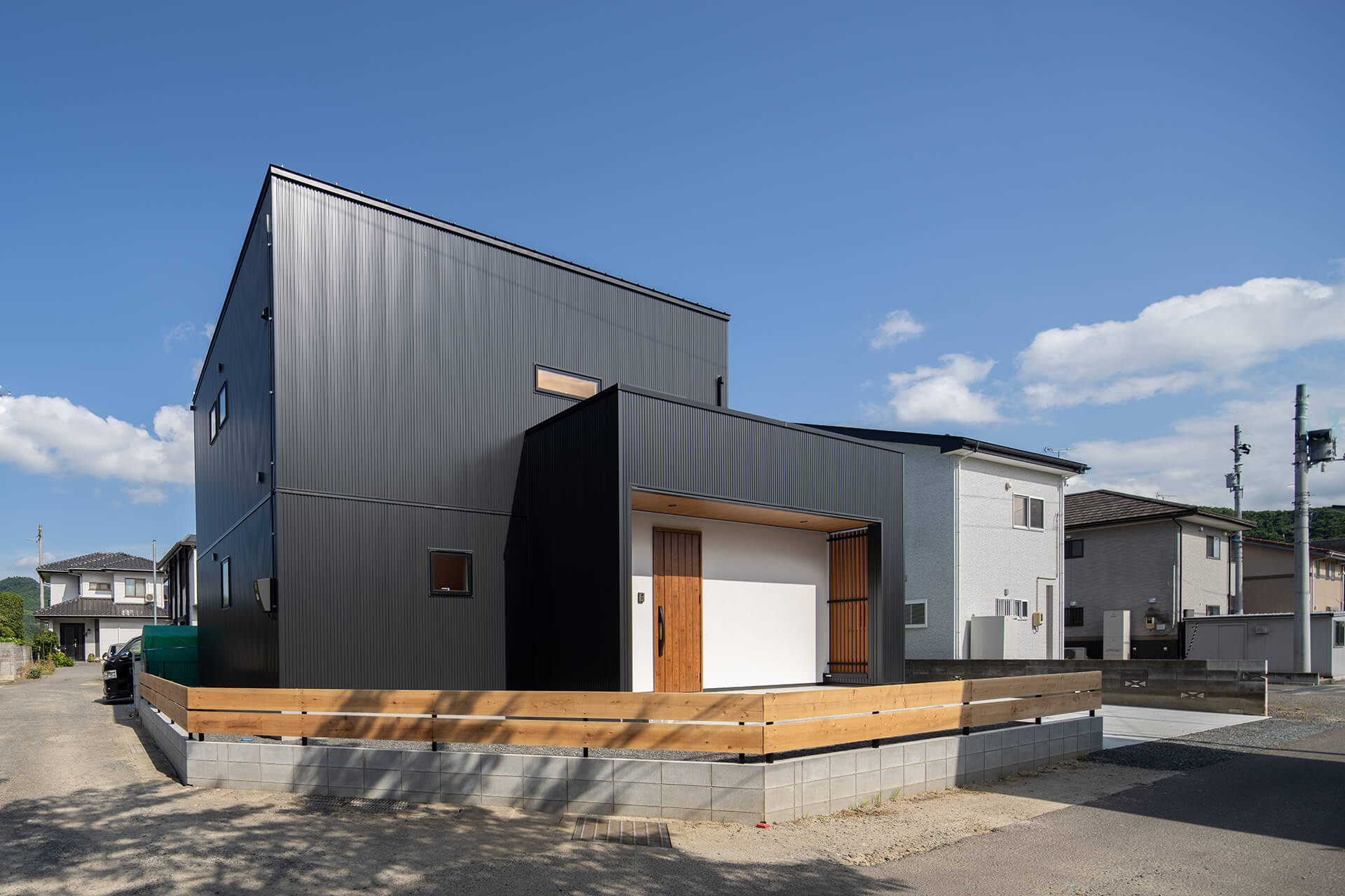 黒のガルバ外壁に塗り壁調玄関周りそして木のコートライン贅沢かつ落ち着きのある外観