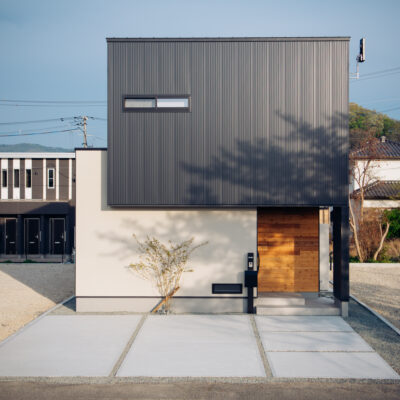陰影が映える、凛とした佇まい。 黒ガルバリウムと塗り壁のコントラストが美しい、シンプルかつ力強いフォルムの住まい。 春には、桜の影がやわらかく壁に揺れ、優しい季節の表情を添えます。
